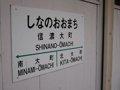 白いプラスチック製のプレートの駅名標。国鉄風だが矢印が緑色になっている。