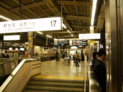 青、赤、白の鮮やかなLED式行先案内板と、床がくすんだ白いタイルのホーム