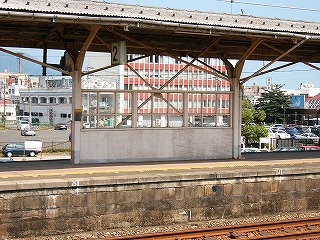 隣のホームの中央にある、9枚のガラスの入った風除け壁。短い壁で、壁の下方はガラスではなく木製。