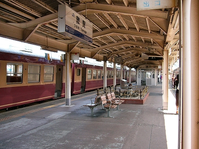 駅名表がぶら下がり、向こうに枯山水が見えるがらんとしたホームに、窓枠のラインは濃いクリーム色でほかはエンジ色の急行形車両が停車している。