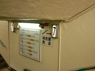 トンネルの突き当たり。突き当りの壁にはまたもや「列車編成案内」がある。写真左には上りの階段。右の階段の数段上に立って撮影。ステンレス枠のふちの幅が広く角が丸みを帯びている7番線を案内する電照式番線表示も壁に取り付けられてある。