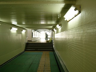 途中数段の階段がある緑の床を持ったホーム下の通路。突き当たりは大きな窓がたり、光が差し込んでいて開放的だ。