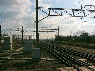 トラス架線柱の下をくぐり遠くで大きく右にカーブする紀勢本線をホームの端から見て。