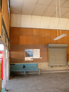 鼠色の古いコンクリートの床面の上におかれた水色の長椅子。その背後は明るい木目調の板張りの壁。