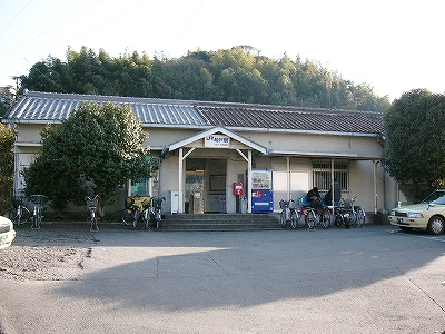 アスファルトの駅前広場と横長の瓦葺の駅舎。
