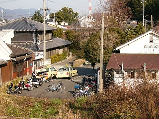 草の土手に囲まれたアスファルトの敷地にタクシーと30台ぐらいの自転車が止まっている。