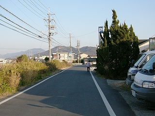 中央線のない道路。自動車の行き来はあまりない。脇には雑草が茂る。