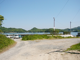 砂地の広場。遠くに軽トラが何台かある。