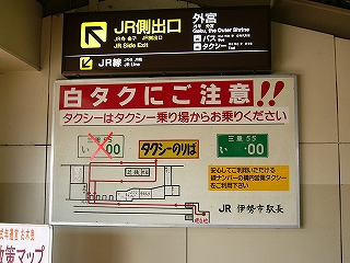 白タク注意喚起の案内板。しろナンバーに赤いばつ印がつけられている。
