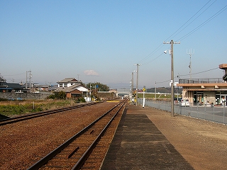 左手に広い線路内。右手にアスファルトと土でハーフになったホーム。遠く左手に一件、右手に一件建物がある。