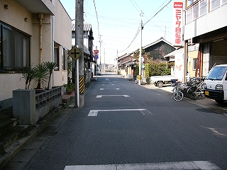 中央線のない古い住宅街の道。左手には古い四角いコンクリートの家。