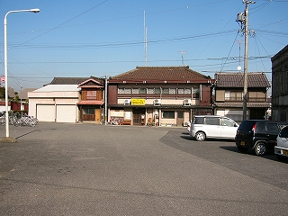 目の前はアスファルトの縦長の敷地、右手には前進駐車された自動車の列、正面奥には並んだ家が三軒。