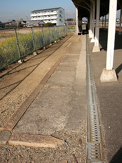 土の地面に浮き出た色つきのコンクリートで縁取りされた白いコンクリートの面。ホームの線路内と反対側にあり、ホームに沿うように長く続いていてホームの壁が現れるところで終わっている。