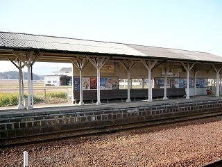 白い柱が二列に渡って三角の上屋を支えるホーム。壁は中途で終わり、終わったところからは冬の田んぼが見えている。