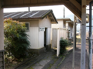 屋根の終わりかける回廊の中から見たトイレ。切妻のコンクリートの古そうな建物。