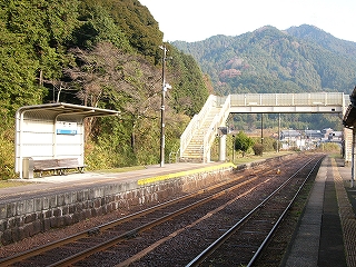 すぐ左手に山が迫る上り線ホーム、線路内。奥には跨線橋があり、背景は緑の高い山。