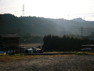 少しだけ高い位置から左手に一軒の田舎の家を見る。狭い畑を挟んだ少し遠くに低い山並みがある。