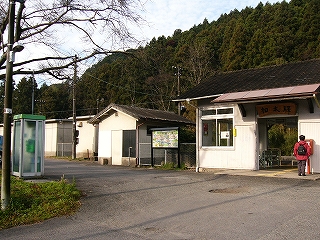 左手に冬枯れした大きな木の一部とその袂の電話ボックス、それらのはすむかいに駅舎。