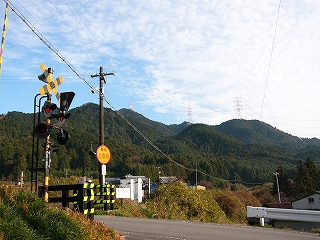 左なめに踏切を見て。ぽこぽこ連なる緑の山々とうろこ雲の青空。