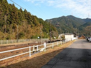 左手に山の木々、その次に停車場、そしそ白い鉄パイプを二本並行させて作った簡単な柵を挟んで道路。道路には人や車は通っていなかった。