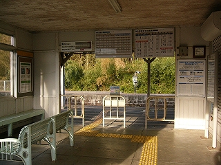奥に広い間口の改札口のある駅舎内のようす。駅舎内の壁と天井は白い木で、床はくすんだコンクリート。改札口の間口からは向かいのホームの緑が見えている。