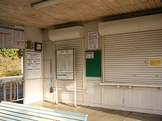 白いシャッターの下りた2つの大きな窓口。窓口は左は縦長で、右は横長になっている。シャッターの閉まった左の窓口の前には時刻表が二本足で立てられている。