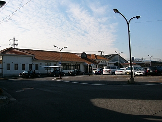オレンジ色の瓦屋根の平屋の駅舎を少し左斜めに見て。駅舎入口の上には小さなファンライトが取り付けられている。