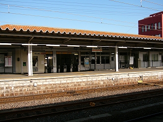 1番線の波板のホーム屋根の下に改札口。波板のホーム屋根の上方にオレンジ色の瓦屋根が見えている。