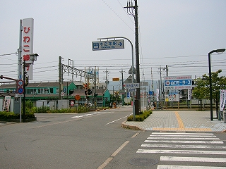 右手に小さな横断歩道、コーナーの幅広の歩道部、少し遠くに踏切。看板や建物の色で色とりどり。