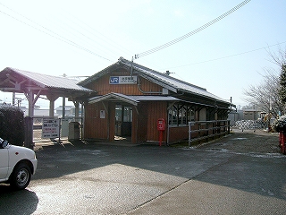 駅舎を斜めに見て。駅舎の右側には土の通路があり、その奥が工事現場になっている。