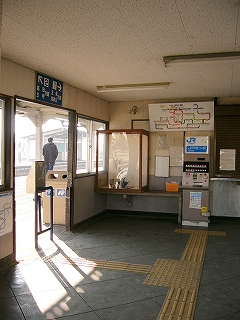 低い載せ台に置かれた生け花と、その隣に設置された縦長の券売機。券売機の上部には路線図運賃表が掲げられている。