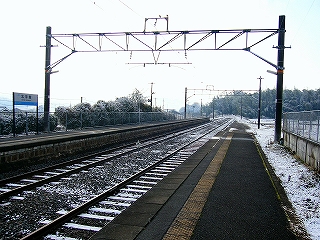 線路内共に伸び行く両ホームは遠くの竹林に突き当たって終わっているらしい風景。大きな門型トラス架線柱が立てられている。線路内も竹林もうっすら雪を被っていて薄暗い感じ。