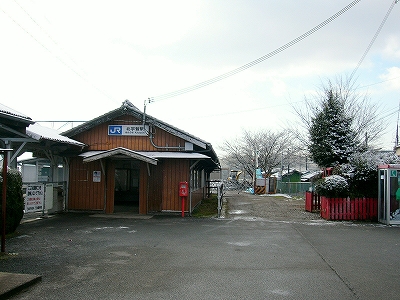 等間隔に黒い縦線の入った薄茶の板の張られた妻面をもつ駅舎。出入り口の間口の上部にも山型の小さな庇がつけられている。