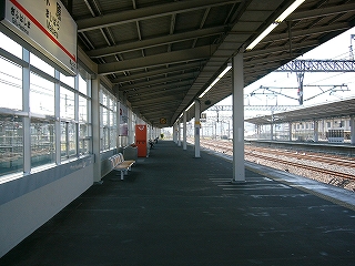 大きな片持ちの上屋下から、ホームの終わりまで見通して。地面はアスファルトで、左の壁は全面枠の入った窓ガラス。とてもすっきりしている。