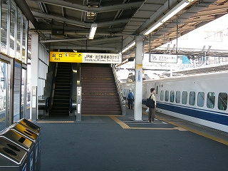 エスカレーターと階段の降り口を見て。右手の12番線に列車が停車中。左の13番線のある側に、全面格子で、それぞれに窓ガラスの入った壁がある。一部分は途切れ、そこを通れば左の13番線のホームの縁に行ける。