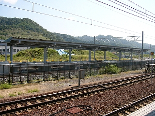 2線の線路内の向こうに新しい造りたてのV字の上屋を持つ島式ホーム。