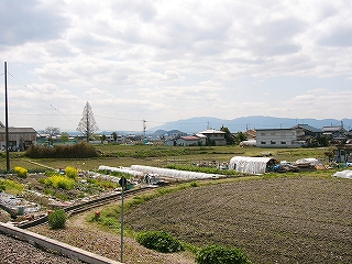 畑。遠くにちらほら民家。ずっと遠くに低い山地。