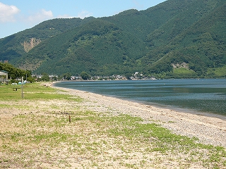 波打際はずっと遠くで険しい緑の山にぶつかることで90度右に向きを変えている。その向きの変わった浜辺沿いに集落が見えている。