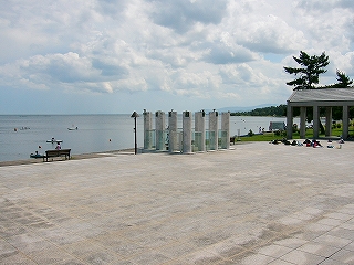 白い石の大きなタイルのはめ込まれた屋外テラス。少し遠くにガラスと石柱で造ったモニュメントもある。