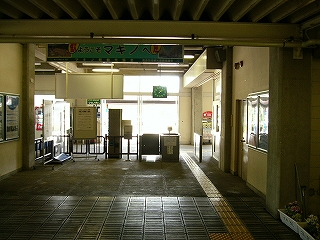 黒いゴムの横棒が入った石板を並べた床面、その先はコンクリート打ち放しの床面の駅舎内。その先に柵と一つのブースでできた改札口。人は誰もいない。