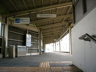 右手にステンレスの手すりの終わり、上方に線路内に向かって上ずった波板の上屋。クリーム色と鼠色が基調となっている。