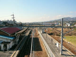 駅舎のある片面ホームと島式ホームを見下ろして。門型架線柱が架線を吊るしている。