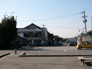 駅前の敷地の中でも宴席に囲まれテーブルと椅子のあるスペースから見た、駅舎前の風景。左奥に民家、右奥に車のＵターンスペース。
