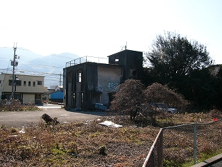 二階建てのコンクリートの小ぶりな建物。コンクリートは汚れ、窓はなく、落書きがされ、廃墟となっている。