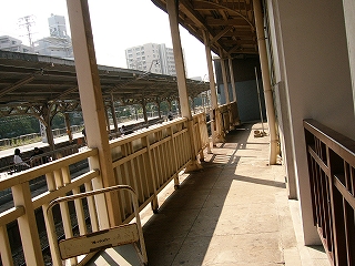 回廊。左にクリーム色の柵。その向こうには低い位置に線路がある。ホームも見えている。