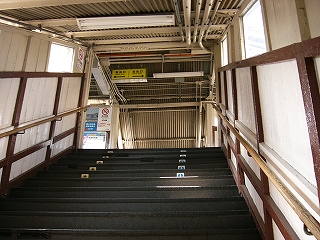 黒い階段から跨線橋の天井を見上げる。上った先は左右に通路が開けているらしい。両脇の壁は白塗りの板に焦げ茶の木枠でできている。