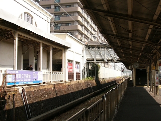 軒を持つ2階分の高さのある白い建物を左手に見て、右に屋根の下の日影のホームを見る。