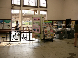 左に焦げ茶の低い柵。その右にパンフレットを陳列する高い棚、そして自動改札。