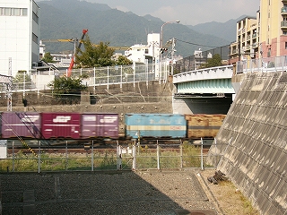貨物列車を真横に見て。右の高い所に灘橋。