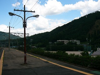 ホーム上の古くて錆びた二股街灯と右手にグラウンドの一部とその奥に校舎二棟を縦に見る。校舎の奥は一つの山。